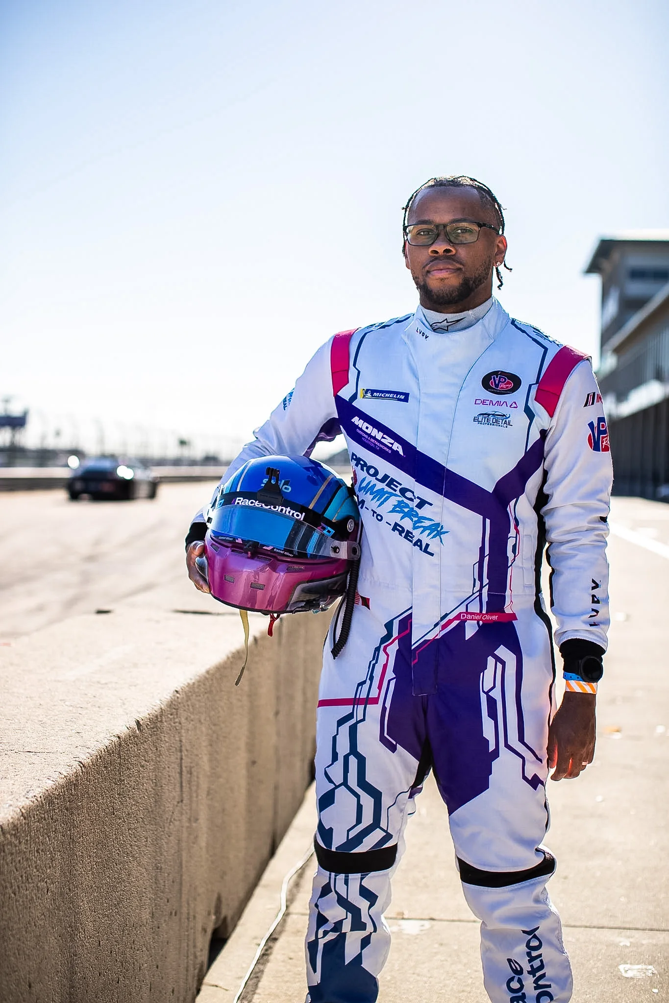 Daniel Oliver standing at the pit wall in his race suit, helmet under his arm