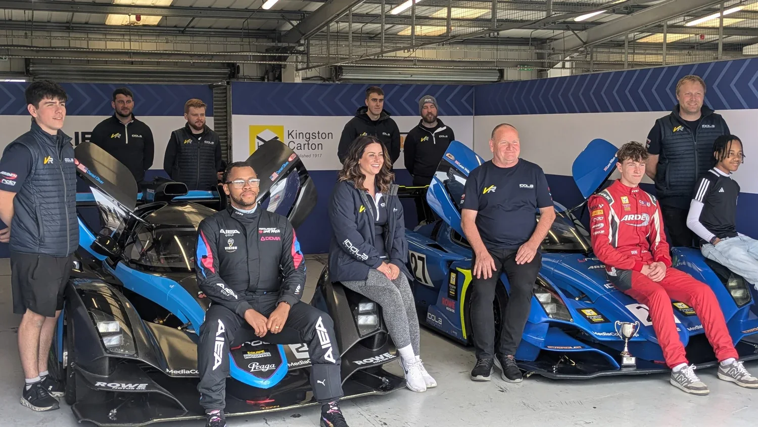 Daniel with the full team of drivers and crew around two Praga prototypes in the garage